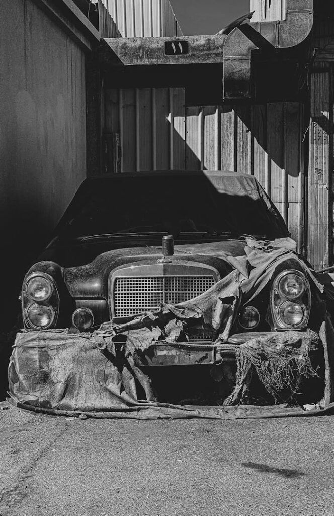 A black and white photo of a vintage abandoned car in an industrial setting.