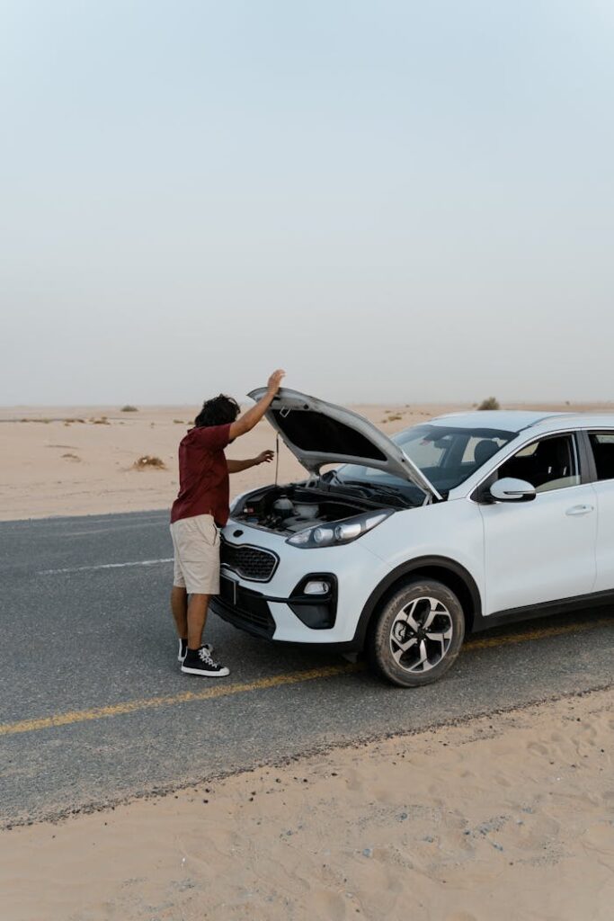 A man inspecting the engine of a car by the roadside in a desert setting.